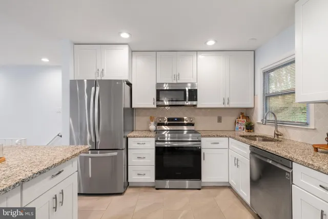 a kitchen with stainless steel appliances granite countertop white cabinets a sink a stove a refrigerator and a granite counter tops