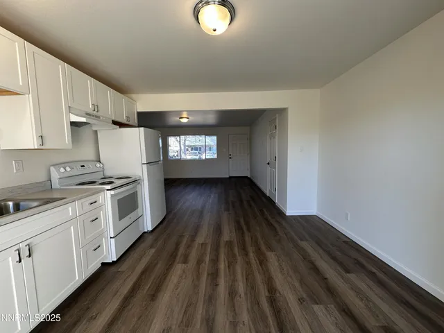 a kitchen with granite countertop a stove a sink and white cabinets with wooden floor