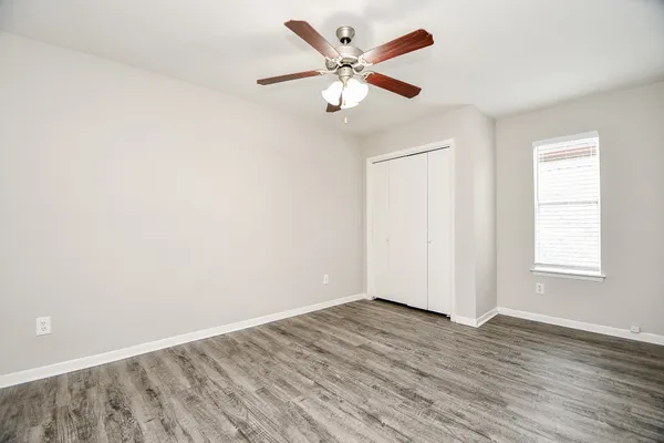 an empty room with wooden floor ceiling fan and window
