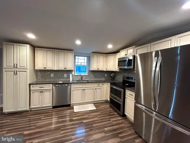 a kitchen with granite countertop stainless steel appliances a refrigerator cabinets and wooden floor