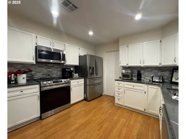 a kitchen with granite countertop a stove top oven a sink dishwasher a refrigerator and white cabinets with wooden floor