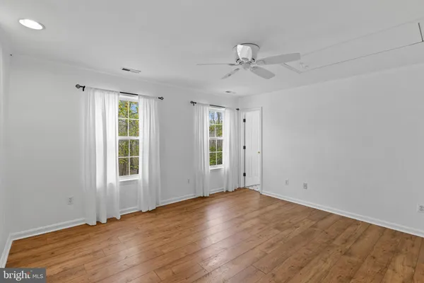 an empty room with wooden floor fan and windows