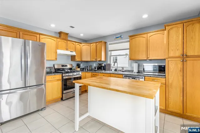 a kitchen with stainless steel appliances granite countertop a refrigerator a sink dishwasher a stove and a dining table with wooden cabinet