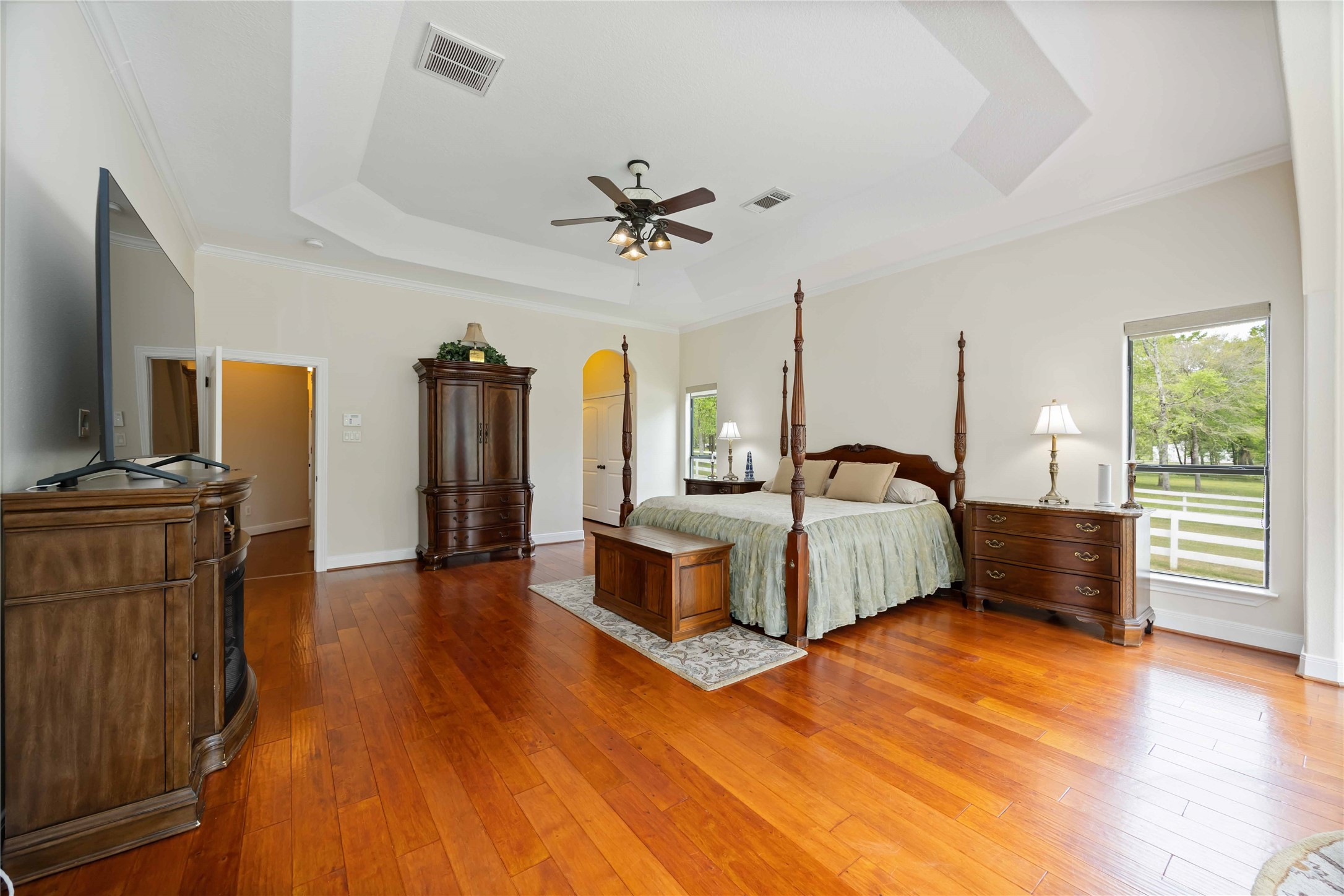 1809 St Beulah Chapel Road Montgomery, TX 77316 - Photo 23 of 50 This spacious bedroom features hardwood floors, a tray ceiling with a fan, and ample natural light from large windows. It includes elegant furniture and offers a serene view of the outdoors.