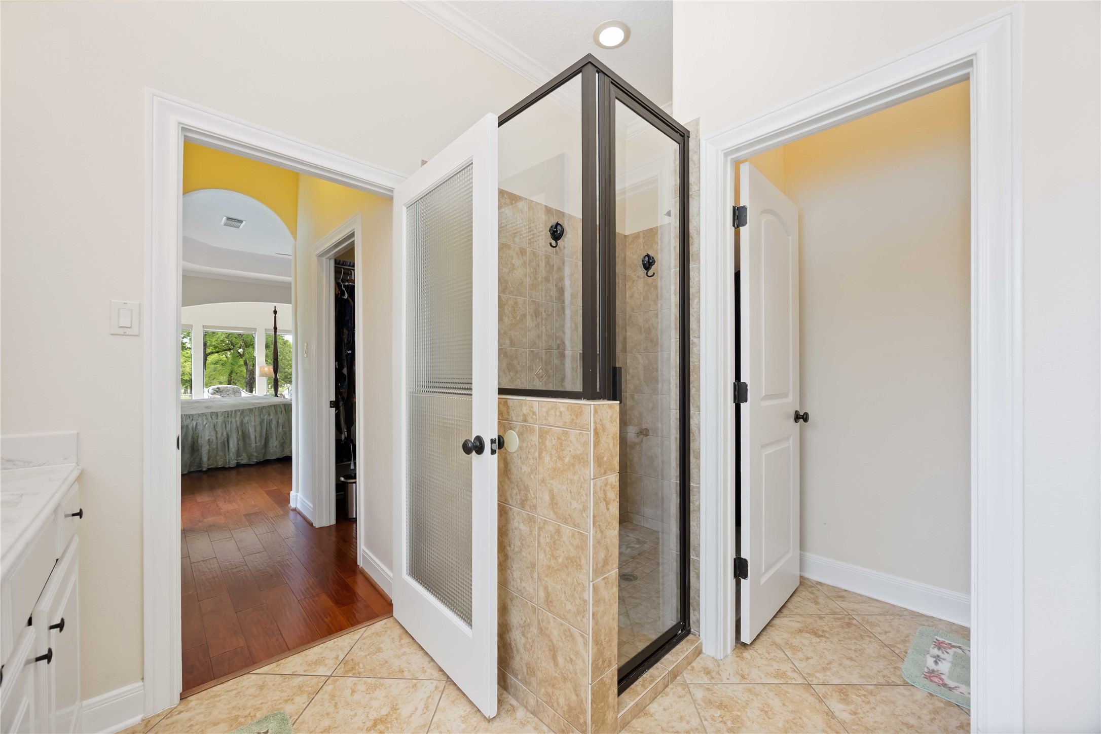 1809 St Beulah Chapel Road Montgomery, TX 77316 - Photo 27 of 50 This photo shows a bathroom with a modern glass-enclosed shower, tiled walls, and a view into a bedroom with hardwood floors and large windows. Bright and inviting, the space offers a seamless flow between the bathroom and bedroom.
