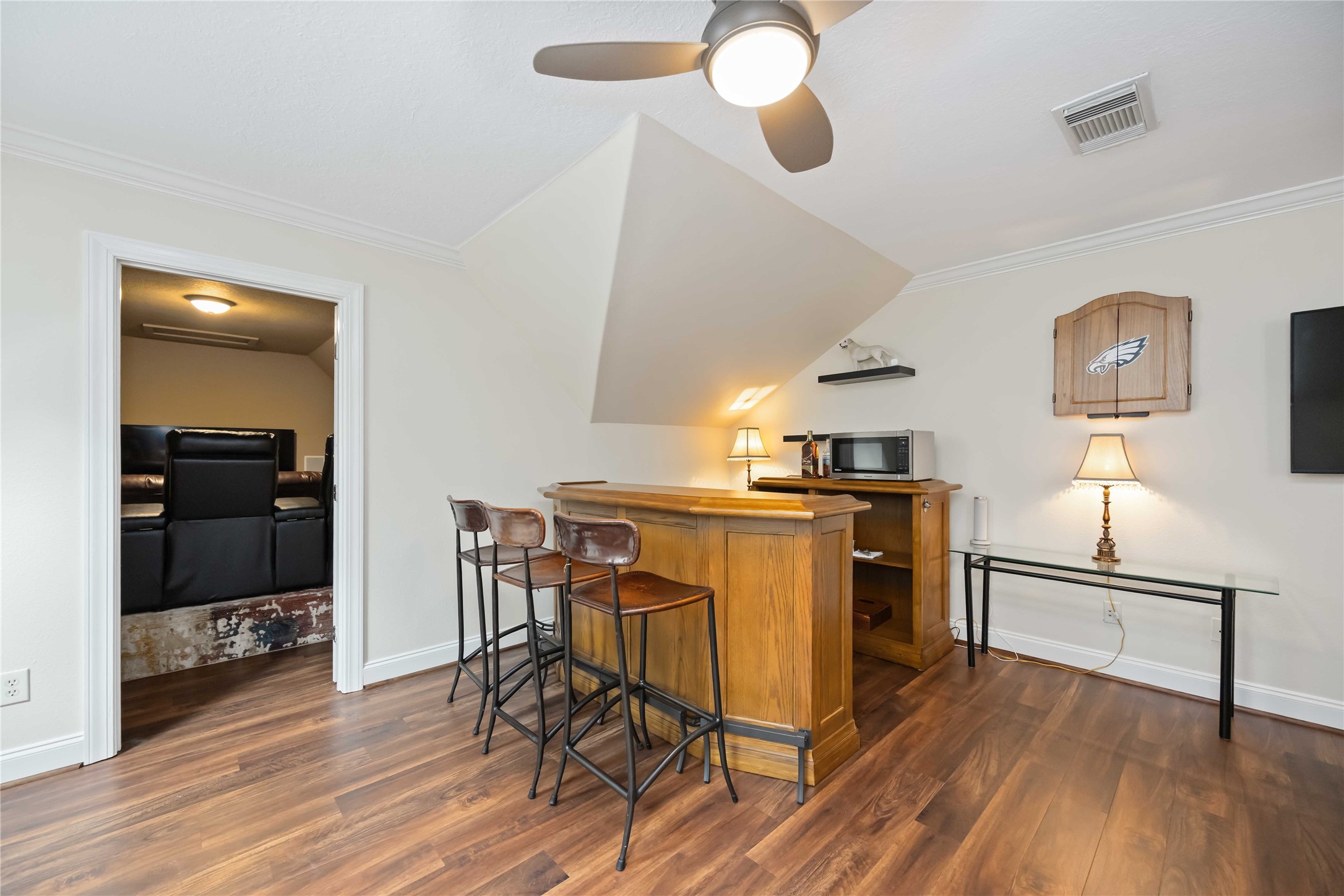 1809 St Beulah Chapel Road Montgomery, TX 77316 - Photo 31 of 50 This cozy space features a small bar area with stools, a microwave, and ample lighting. Adjacent is a room with comfortable seating, ideal for entertainment. The room has wood flooring, a ceiling fan, and a modern aesthetic.