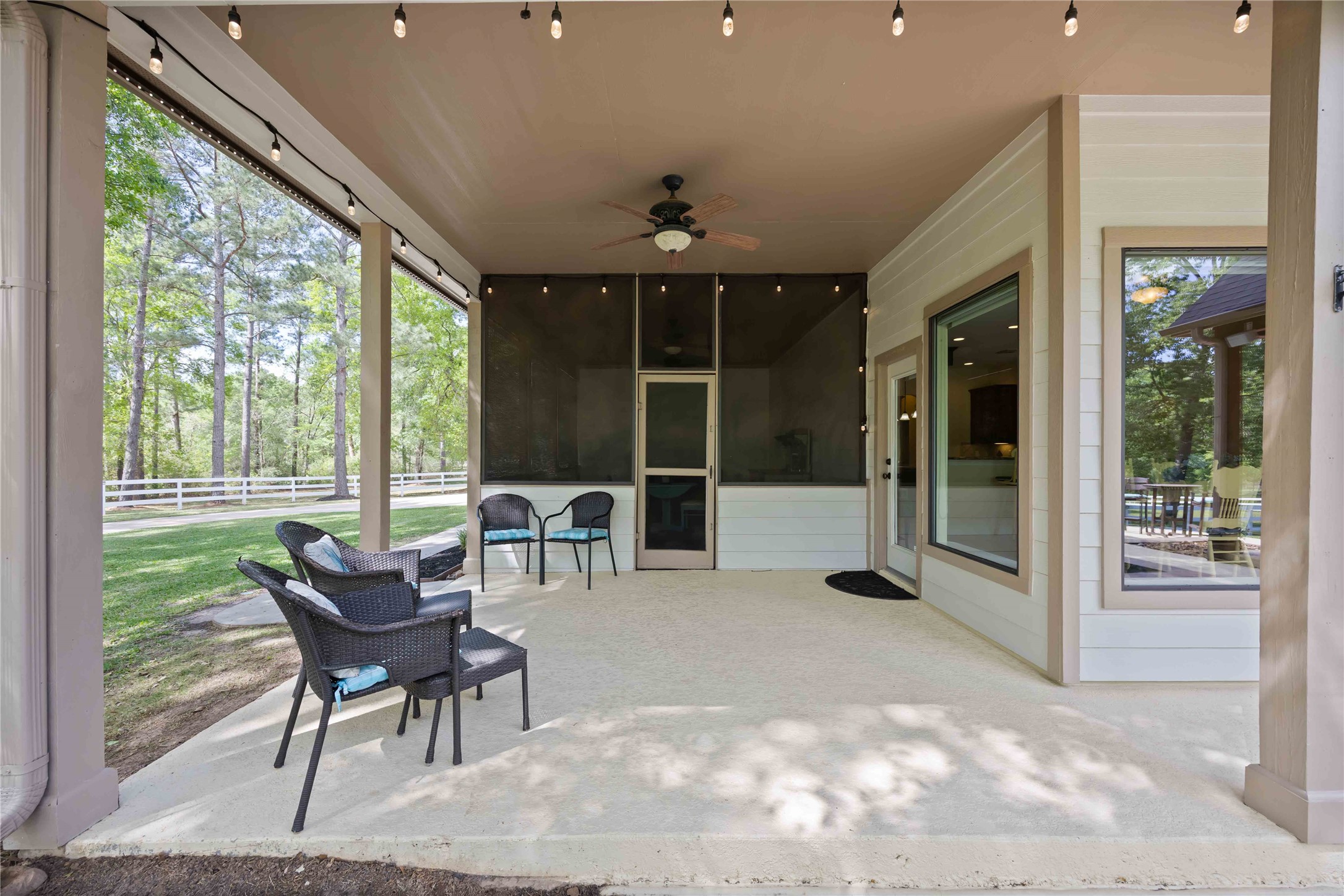1809 St Beulah Chapel Road Montgomery, TX 77316 - Photo 35 of 50 This inviting outdoor patio features a covered space with string lights and a ceiling fan, offering a cozy seating area with a view of lush greenery. It's perfect for relaxing or entertaining in a serene setting.