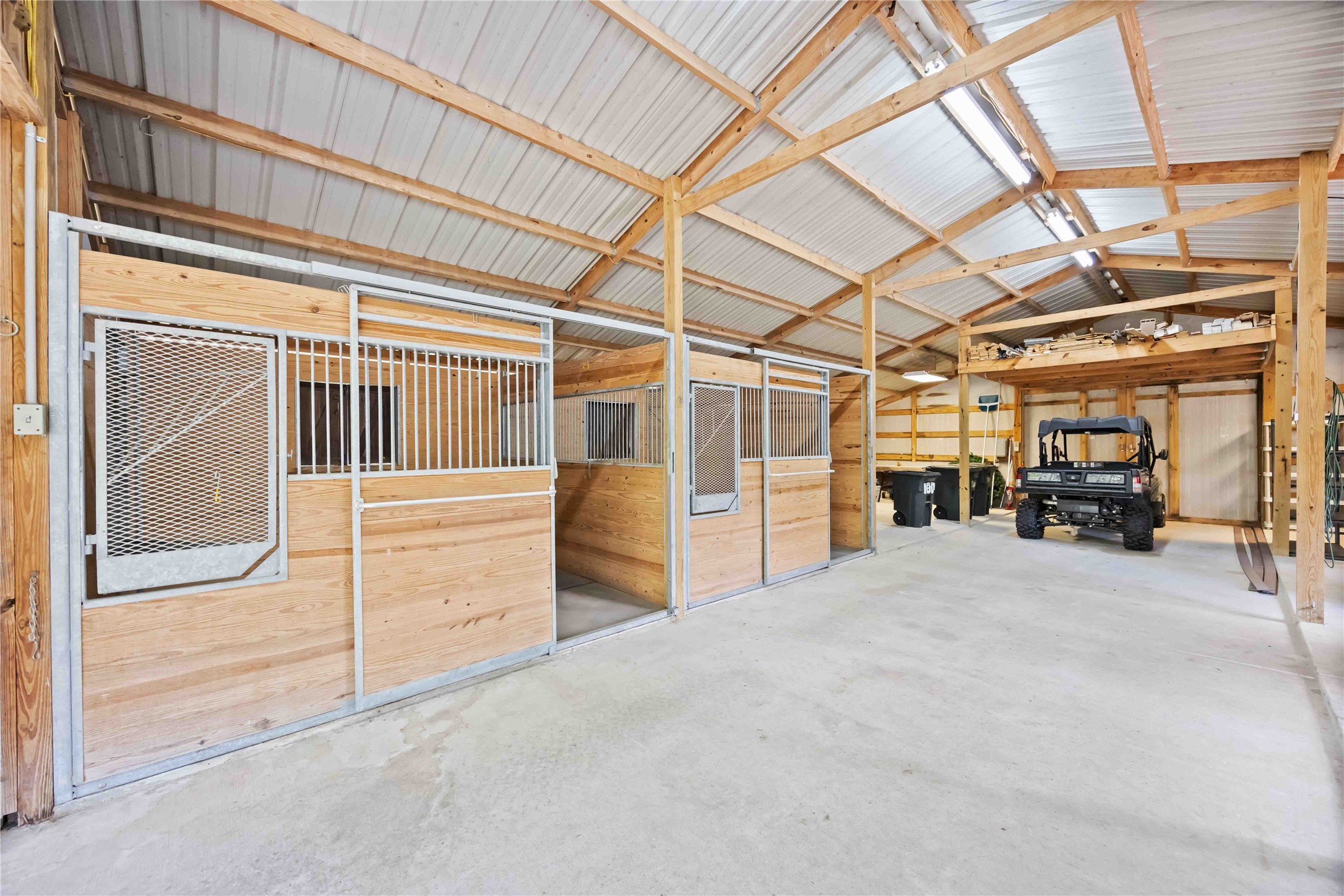 1809 St Beulah Chapel Road Montgomery, TX 77316 - Photo 44 of 50 This photo shows a spacious, well-lit barn with wooden stalls and a concrete floor, ideal for housing animals or storage, featuring high ceilings and a vehicle parked inside.