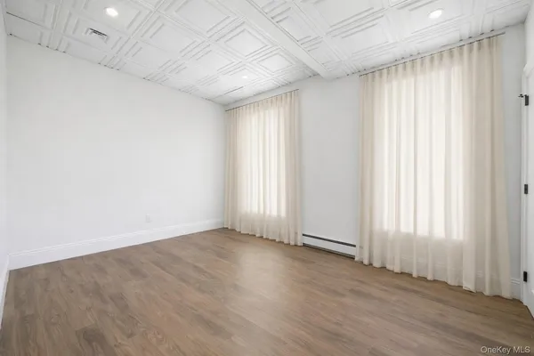 an empty room with wooden floor and windows with curtains