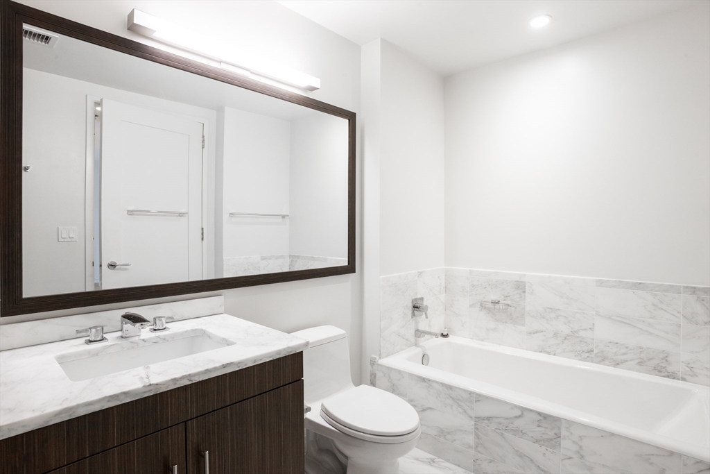 580 Washington Street, Unit 304 Boston, MA 02111 - Photo 18 of 18 a bathroom with a bathtub shower sink vanity mirror and toilet