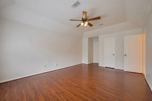 an empty room with wooden floor fan and windows