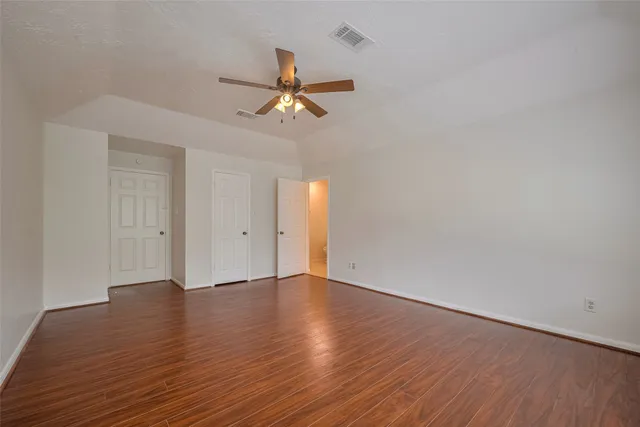 a view of an empty room with wooden floor and a ceiling fan