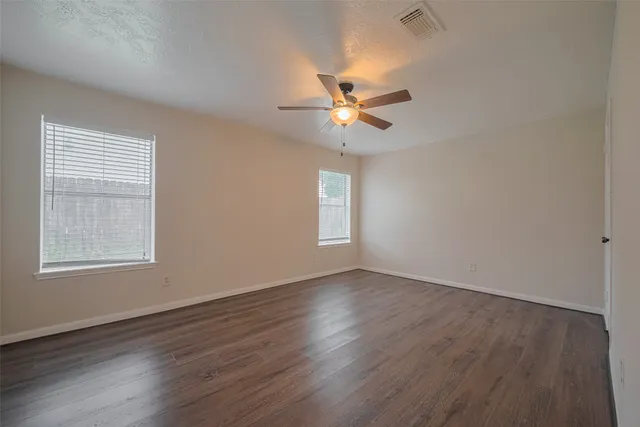 an empty room with wooden floor fan and windows