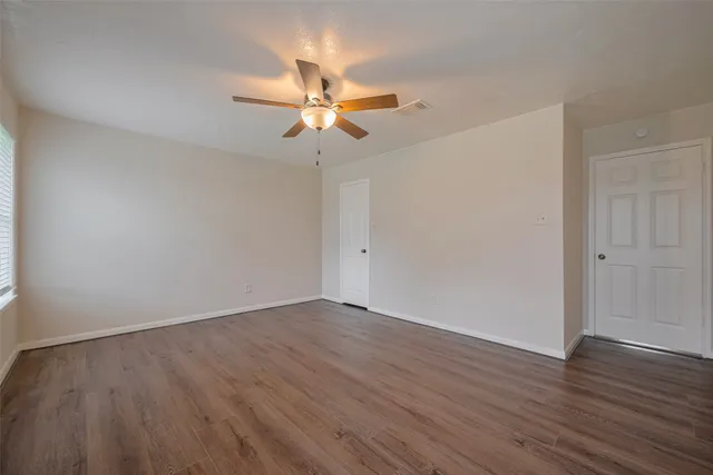 an empty room with wooden floor fan and windows