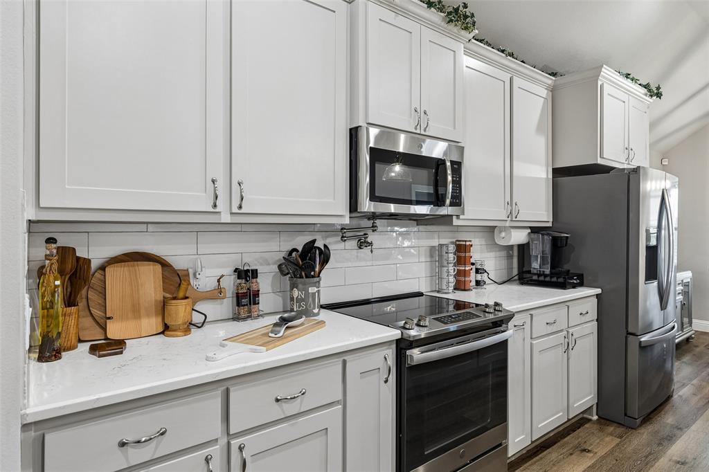 108 Maverick Lane Pilot Point, TX 76258 - Photo 9 of 27 Kitchen featuring white shaker-style cabinetry, stainless steel appliances, a subway tile backsplash, light-toned countertops, and wood-finish flooring