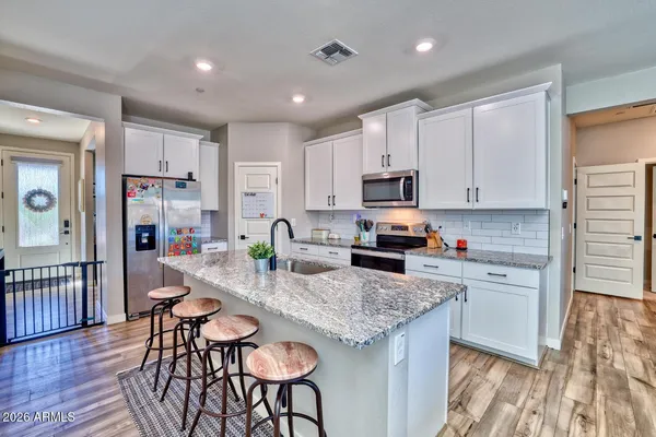 a kitchen with stainless steel appliances granite countertop a stove top oven a refrigerator a sink and white cabinets with wooden floor