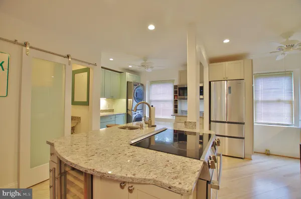 a kitchen with stainless steel appliances granite countertop a refrigerator a oven and white cabinets with wooden floors