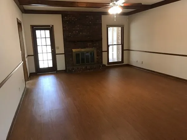 an empty room with wooden floor fireplace and windows