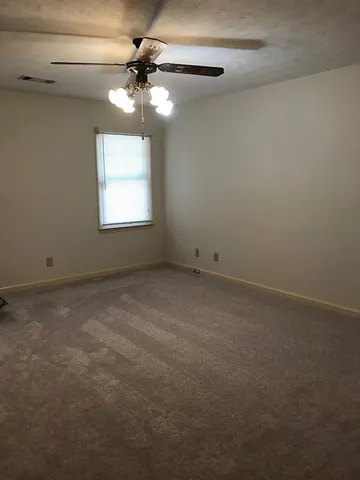 an empty room with a chandelier fan and windows