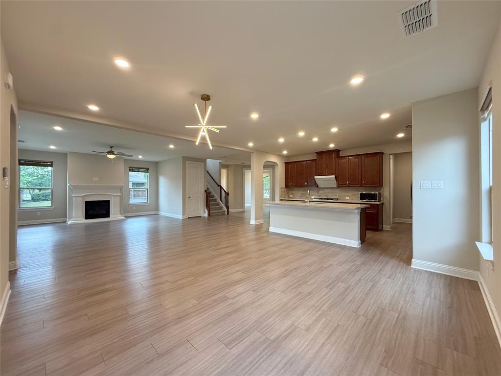 9829 Sharps Road Frisco, TX 75035 - Photo 10 of 40 Unfurnished living room featuring arched walkways, a fireplace with raised hearth, light wood-style flooring, and recessed lighting
