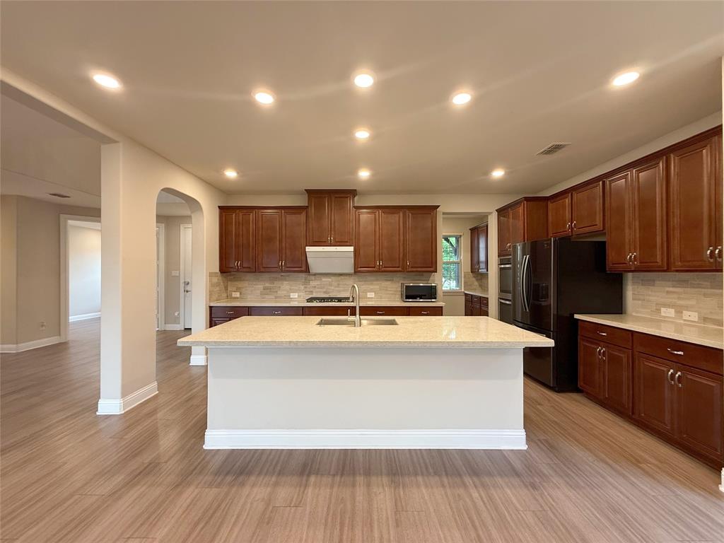 9829 Sharps Road Frisco, TX 75035 - Photo 11 of 40 Kitchen featuring arched walkways, stainless steel appliances, a center island with sink, light stone countertops, and recessed lighting