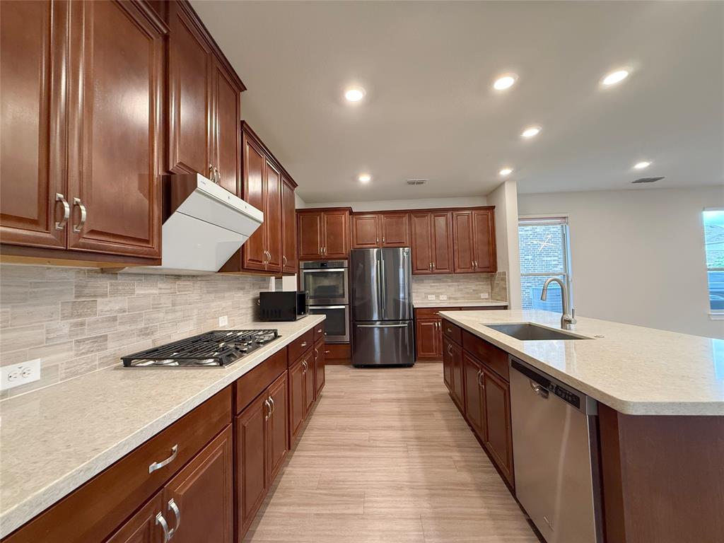 9829 Sharps Road Frisco, TX 75035 - Photo 12 of 40 Kitchen featuring stainless steel appliances, recessed lighting, light stone counters, an island with sink, and decorative backsplash