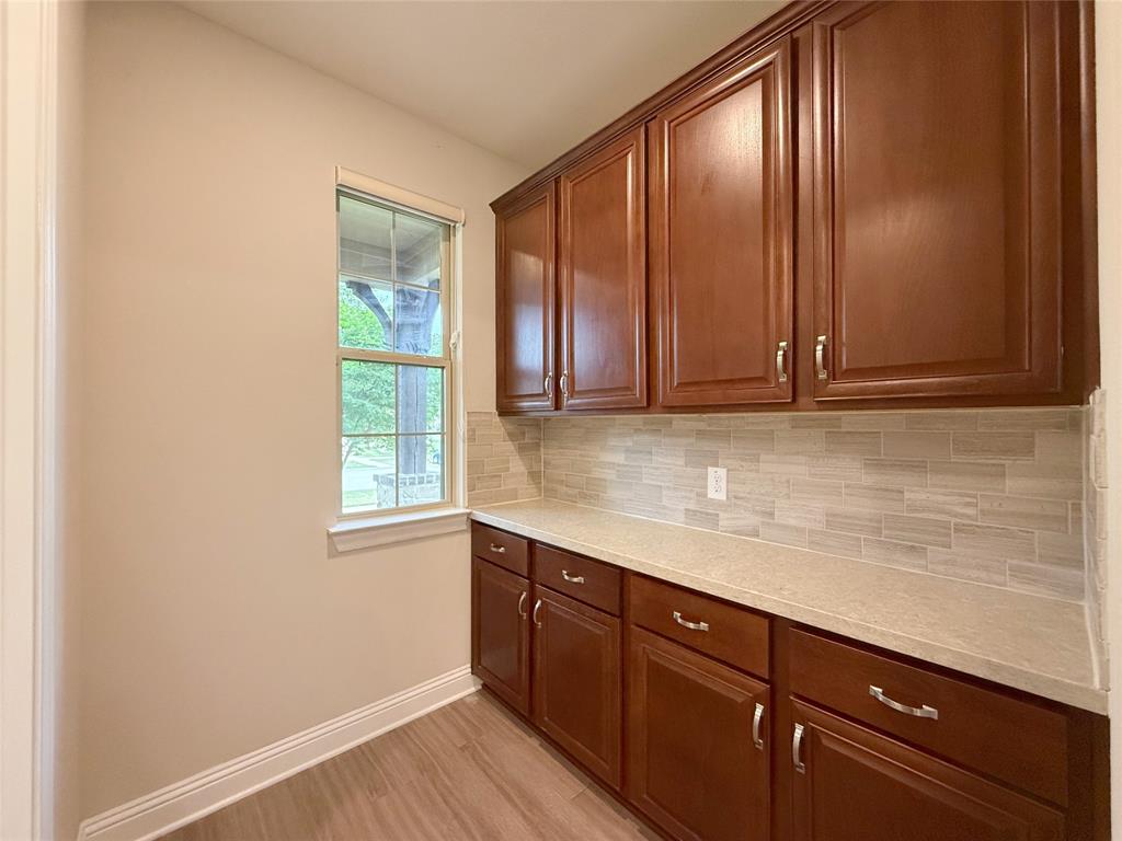 9829 Sharps Road Frisco, TX 75035 - Photo 14 of 40 Kitchen with light stone countertops, light wood finished floors, wood finish cabinetry, and tasteful backsplash