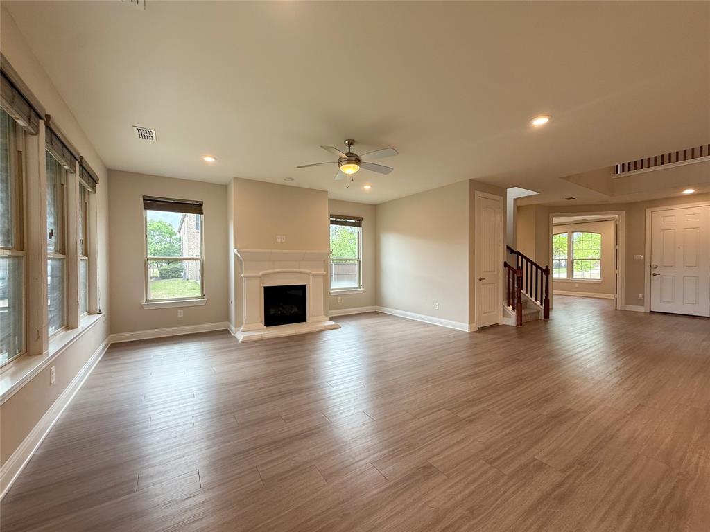 9829 Sharps Road Frisco, TX 75035 - Photo 6 of 40 Unfurnished living room featuring a fireplace with raised hearth, wood finished floors, a ceiling fan, and recessed lighting