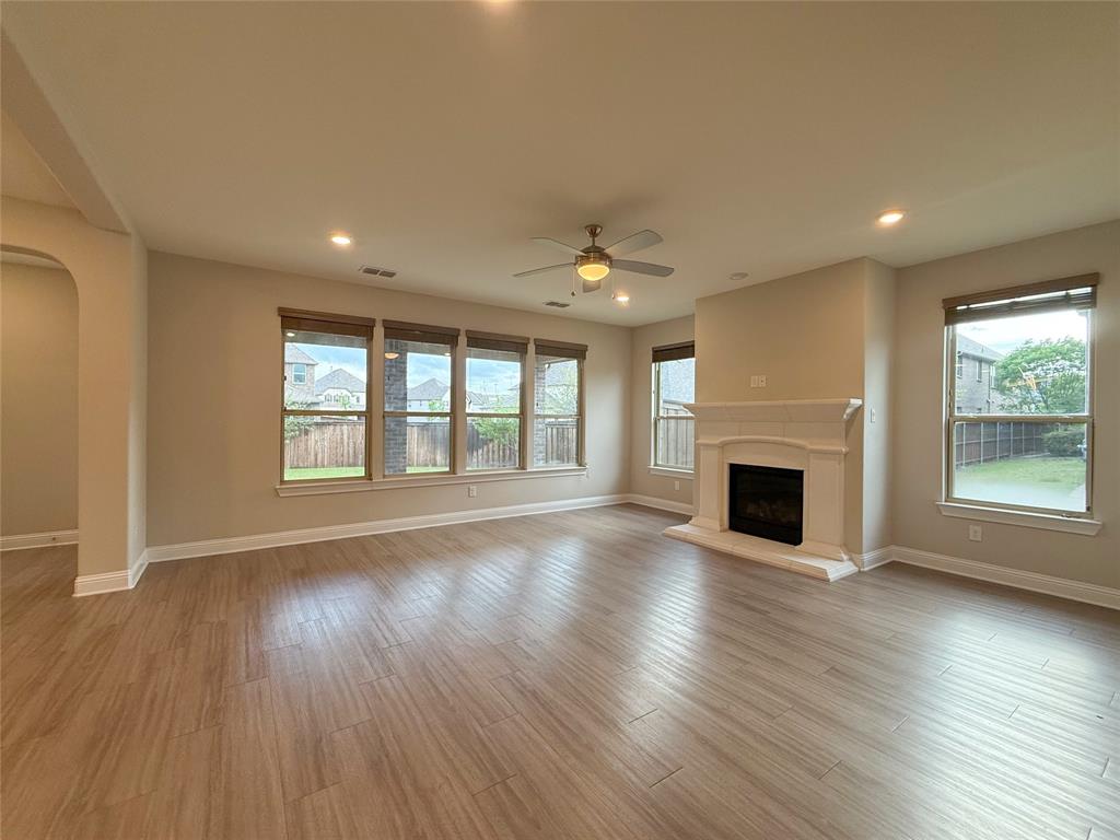 9829 Sharps Road Frisco, TX 75035 - Photo 8 of 40 Unfurnished living room with arched walkways, a ceiling fan, a fireplace with raised hearth, light wood-style flooring, and plenty of natural light