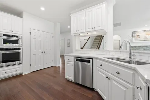 a kitchen with stainless steel appliances granite countertop a stove a sink and white cabinets with wooden floor