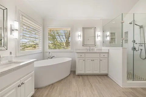 a spacious bathroom with a double vanity sink a mirror a bathtub and next to a window