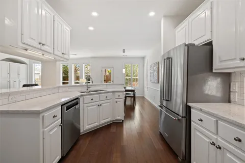 a kitchen with stainless steel appliances granite countertop a refrigerator a sink dishwasher a stove and white countertops with wooden floor