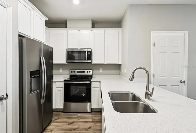 a kitchen with stainless steel appliances granite countertop a refrigerator a sink a stove and white cabinets