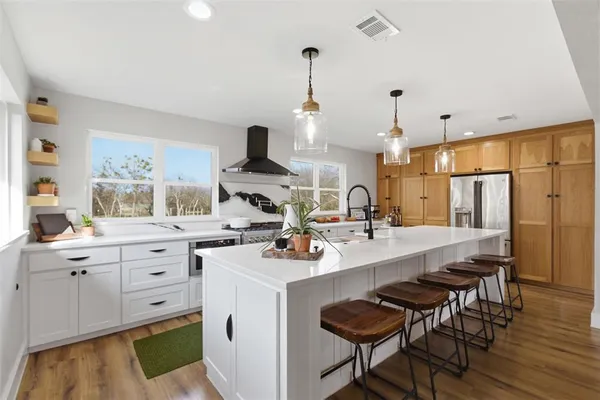 a kitchen with stainless steel appliances kitchen island granite countertop a sink stove and white cabinets with wooden floor