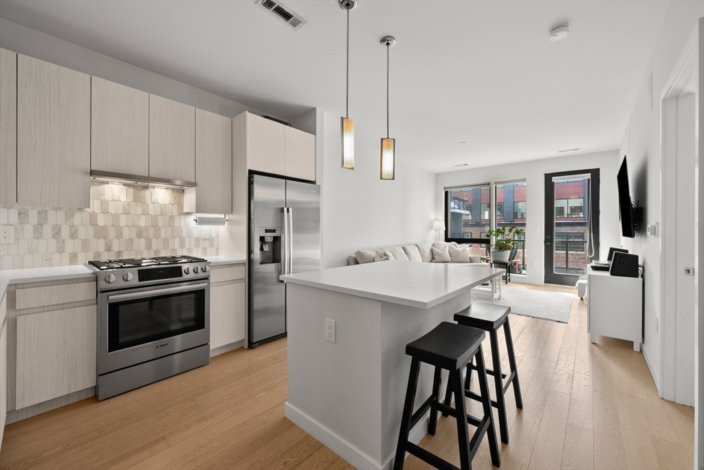 45 West 3rd Street, Unit 406 Boston, MA 02127 - Photo 4 of 14 a kitchen with stainless steel appliances kitchen island a table chairs refrigerator and sink
