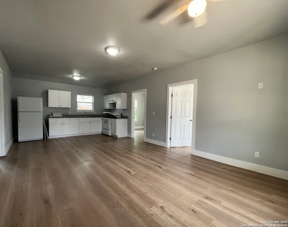 an empty room with wooden floor kitchen view and windows