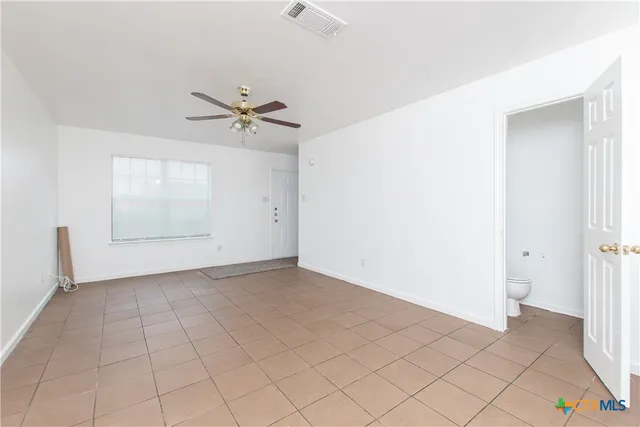an empty room with chandelier fan and windows