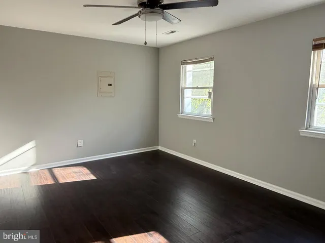 an empty room with wooden floor fan and windows