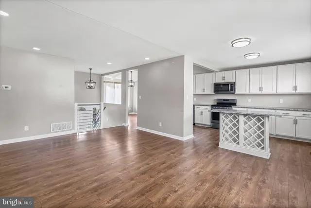 a kitchen with stainless steel appliances kitchen island granite countertop a refrigerator a stove a sink and white cabinets with wooden floor