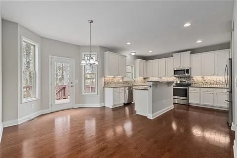 an empty room with wooden floor chandelier and windows