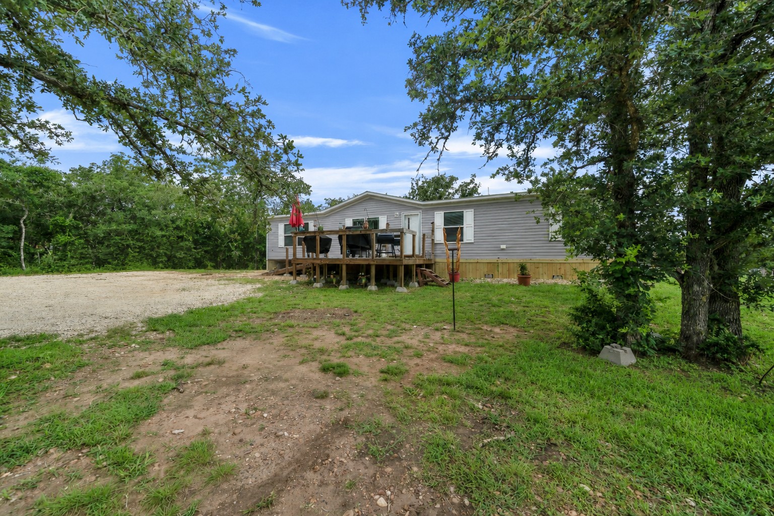 2755 Washburn Road Luling, TX 78648 - Photo 7 of 40 A welcoming front deck extends from this comfortable single-story residence, framed by mature trees and a gravel driveway.