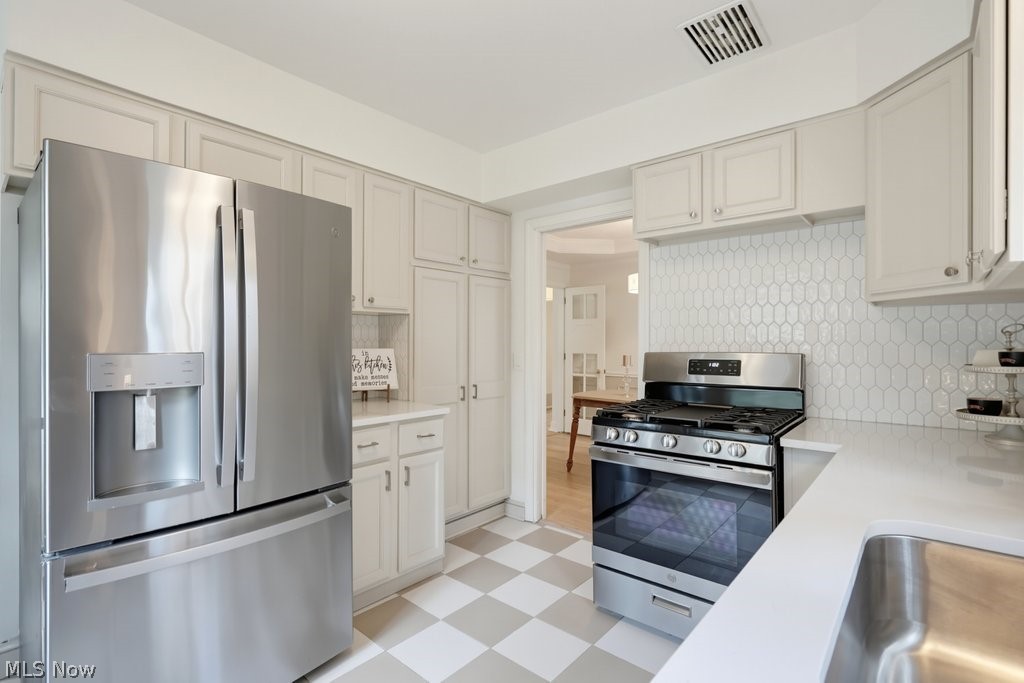 2468 Ridgewood Road Akron, OH 44313 - Photo 18 of 50 Stainless steel appliances, white cabinetry with silver hardware, patterned tile backsplash, solid surface countertops, and checkered tile flooring