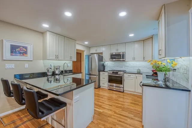 a open kitchen with stainless steel appliances granite countertop a stove top oven a sink dishwasher a dining table and chairs with wooden floor