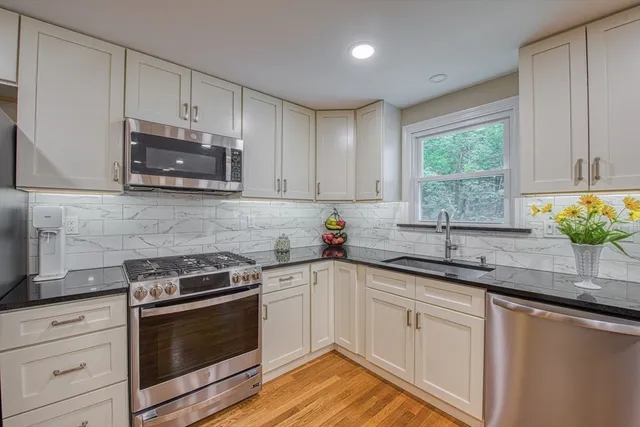 a kitchen with granite countertop white cabinets appliances a window and a sink