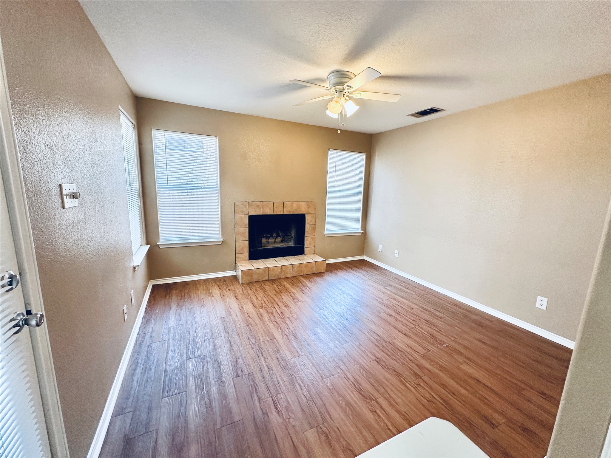 8814 Schick Road, Unit B Austin, TX 78729 - Photo 12 of 36 Unfurnished living room featuring plenty of natural light, wood finished floors, a tiled fireplace, ceiling fan, and a textured wall