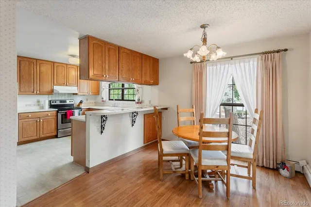 a open kitchen with stainless steel appliances granite countertop a stove top oven a refrigerator a dining table and chairs with wooden floor