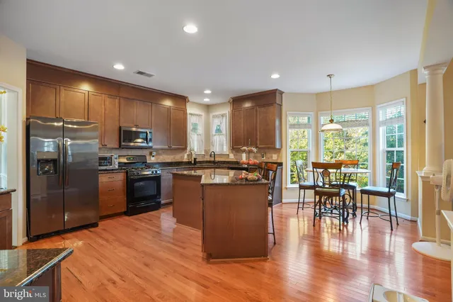 a kitchen with stainless steel appliances granite countertop a refrigerator a stove top oven and a dining table with wooden floor