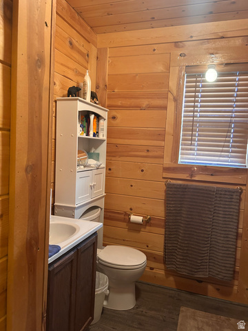 19075 West Honesty Cove Duchesne, UT 84021 - Photo 14 of 44 Bathroom featuring wood paneling throughout, a vanity with a white countertop and basin, a toilet, a window with blinds, and wood-finish flooring