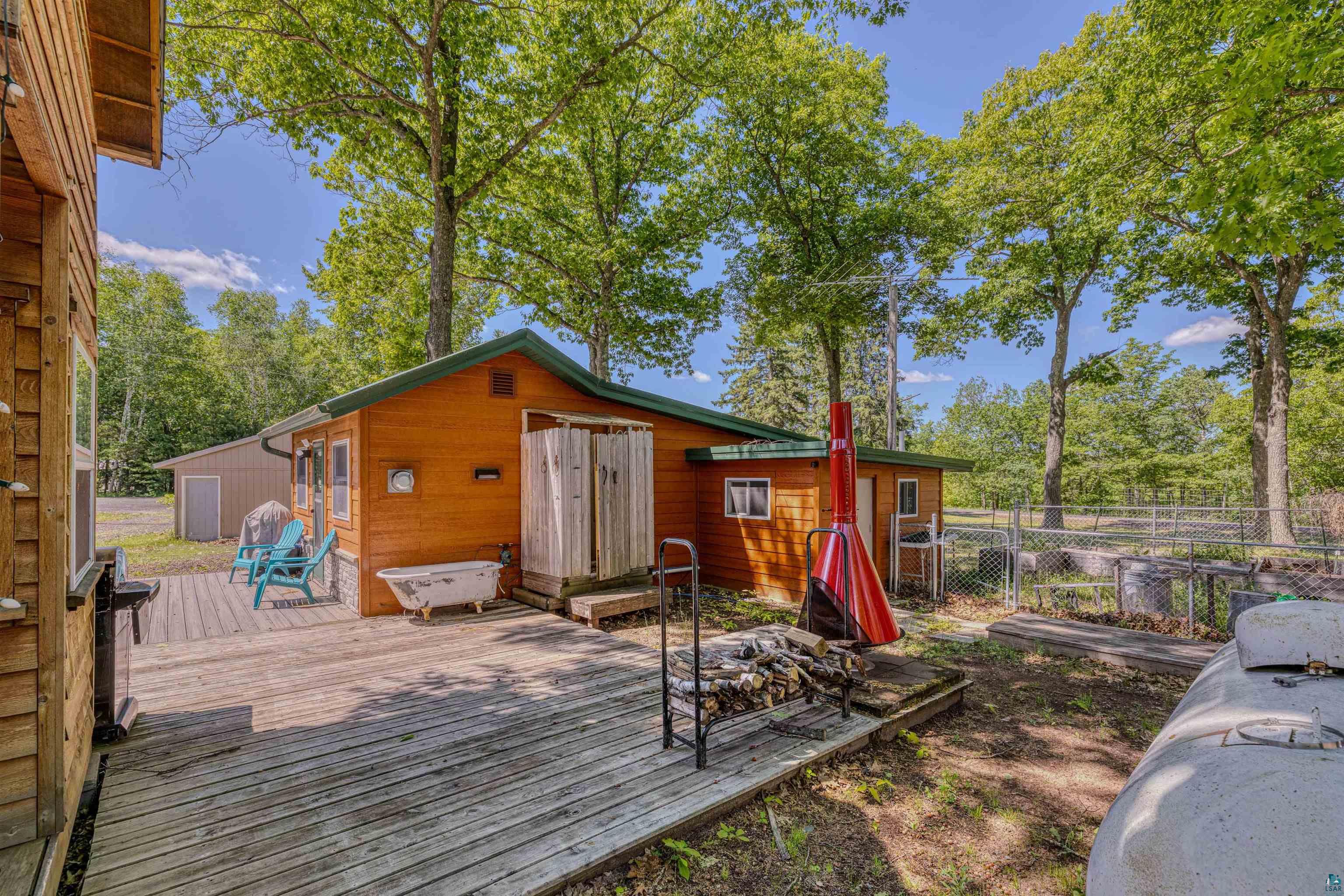 66075 Rooster Road Iron River, WI 54847 - Photo 35 of 52 Expansive outdoor decking featuring a rustic wood-sided structure with a green trim roof, surrounded by mature trees
