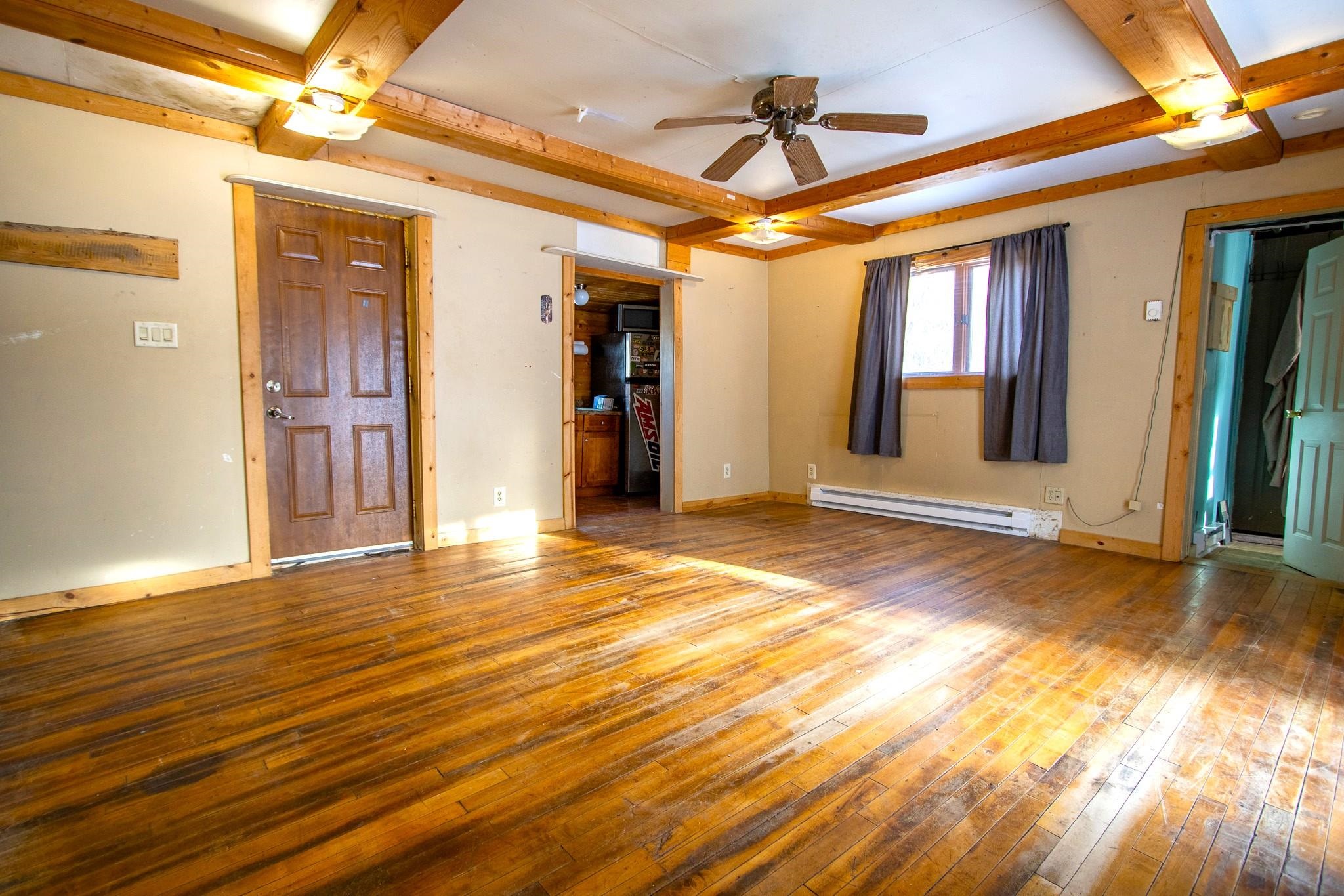 3946 East Calvary Road Duluth, MN 55803 - Photo 5 of 12 Unfurnished living room featuring wood-type flooring, beam ceiling, a baseboard heating unit, and a ceiling fan